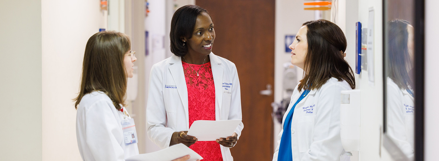 Three medical professionals in white coats having a discussion in a hospital hallway. Three medical professionals in white coats having a discussion in a hospital hallway.